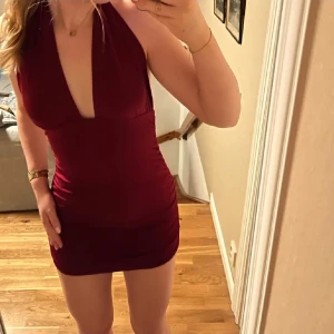 Vinröd klänning med djup urringning - Snygg vinröd kortklänning med djup urringning och öppen rygg. Perfekt för en utekväll eller fest. Klänningen har en tight passform som framhäver figuren.