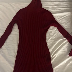 Vinröd ribbad klänning - Snygg vinröd ribbad klänning med långärmad design och polokrage. Perfekt för kyligare dagar med sin mysiga och stilrena look. Passar utmärkt för både vardag och festliga tillfällen.