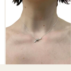 Silverhalsband med hjärthänge från Lotta Hasselblad  - Elegant silverhalsband med ett hjärthänge och en pil från Lotta Hasselblad . Perfekt för att ge en subtil men stilfull touch till din outfit. Kedjan är tunn och smidig, vilket gör den bekväm att bära hela dagen. 