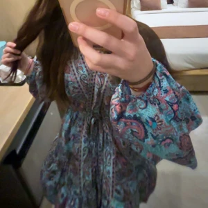 Mönstrad klänning med vida ärmar - Säljer en färgglad klänning som jag köpte utomlands med ett livligt mönster i blått och rosa. Klänningen har vida ärmar och ett knytband i midjan❤️