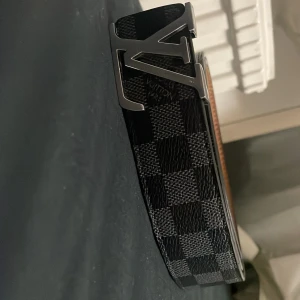 Svart rutigt bälte från Louis Vuitton - Snyggt svart bälte från Louis Vuitton. Logan behöver 2 skruvar men fortfarande är bältet i bra skick