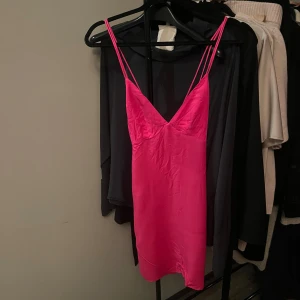 Rosa axelbandslös klänning - Snygg rosa klänning med smala axelband och v-ringning. Klänningen har en öppen rygg med korsade banddetaljer. Perfekt för en somrig look.