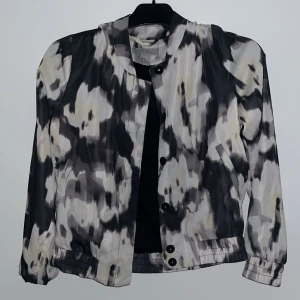 Mönstrad jacka med knappar - Säljer en cool jacka med abstrakt mönster i svart, grått och vitt. Jackan har knappar framtill och långa ärmar. Perfekt för att ge din outfit en unik touch!