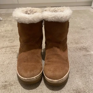 Bruna mockaboots liknande UGGS med fluff i!  - Säljer ett par bruna boots i mocka med mjukt vitt foder. De har en dragkedja på sidan (skriv om ni vill ha bilder på den!) Skorna är i storlek 35 och har använts, jag tror två vintrar för några år sedan! Skorna är från PAX. Skriv för fler bilder och pris kan diskuteras! Jag har lagt strumpor i skorna så att de håller sin form bättre då det stått i min garderob länge och blivit lite sena i den övre delen! 