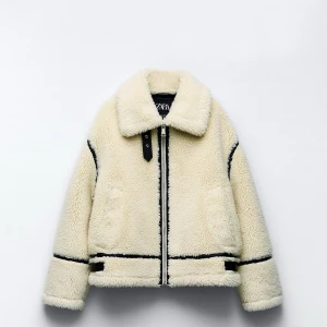 Naturvit teddyjacka från Zara - Mysig naturvit teddyjacka från Zara med svarta detaljer. Jackan har en dragkedja framtill och en klassisk krage. Perfekt för kyliga dagar med sin fluffiga och varma design. Oversized passform, sitter fint oavsett om man är strl XS-M. Ord pris 1200