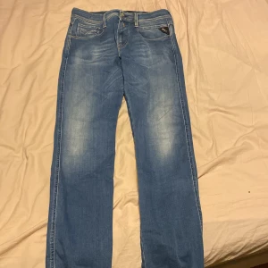 Blå jeans från Replay - Snygga blå jeans från Replay med en klassisk femficksdesign och diskret slitageeffekt. De har en knappgylf och bälteshällor, vilket gör dem perfekta för en avslappnad stil. Märket Replay syns tydligt på baksidan. 32 i längd
