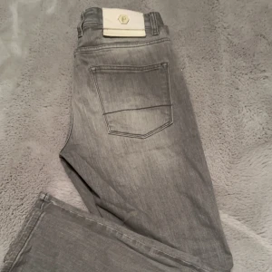 LFPF - Snygga grå jeansbyxor från LFPF med en klassisk femficksdesign. Byxorna har en diskret logga på bakfickan och en knappgylf. Perfekta för en stilren look.