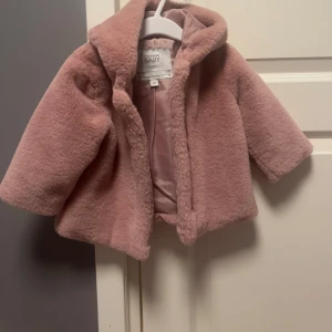 Rosa teddyjacka från Mywear Baby - Söt rosa teddyjacka från Mywear Baby med huva. Perfekt för att hålla de små varma och mysiga. Jackan har långa ärmar och är gjord i ett mjukt material som känns skönt mot huden.