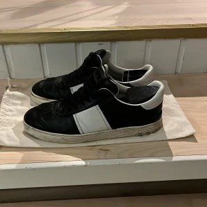 Valentino flycrew  - Snygga svartvita sneakers från Valentino med klassisk design. Skorna har en vit rand på sidan och svarta snören. Perfekta för en stilren look. Ända defekten är att dom har tappat några spikar 40-41