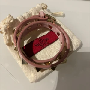 Rosa dubbel armband från Valentino - Snyggt rosa armband från Valentino med guldiga pyramidformade nitar. Armbandet är designat för att lindas runt handleden och har en justerbar stängning. Perfekt för Stockholmsstil o passar allt. Säljs inte längre är one of a kind