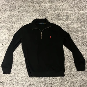 Svart tröja med dragkedja från Ralph Lauren - Säljer en stilren svart tröja från Ralph Lauren med en halv dragkedja framtill. Tröjan har långa ärmar och en liten röd logotyp på bröstet. Ägt den ett tag nu men skicket är bra