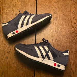 Adidas L.A. Trainer sneakers - Snygga Adidas L.A. Trainer sneakers i marinblått med vita detaljer och klassiska tre ränder. Skorna har en unik sula med små dubbar för extra grepp och komfort. Tillverkade i en kombination av mocka och syntetmaterial, perfekt för trainers inför vintern nu.  Bara använda 10 ggr