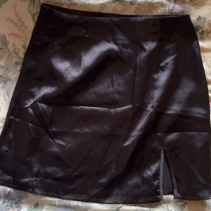 Svart satin kjol  - Snygg svart satin kjol från Shein med en elegant slits framtill. Perfekt för att ge en stilren look. Kjolen har en glansig finish som ger en lyxig känsla.