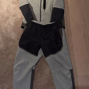 Grå  Nike dress  - Säljer en grå hoodie från Nike med svarta detaljer och dragkedja. Perfekt för träning eller en avslappnad dag. Hoodien har en stilren design med Nike-loggan på bröstet.