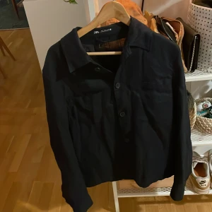 Svart jacka från Zara - Säljer en stilren jacka från Zara med knappar framtill. Jackan har en klassisk krage och långa ärmar, perfekt för en minimalistisk look. Passar bra till både vardag och mer uppklädda tillfällen.