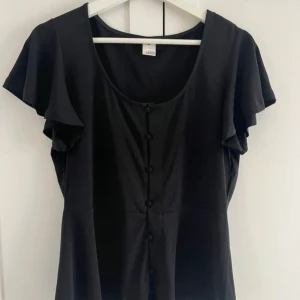 Svart blus med knappar - Snygg svart blus från H&M med korta ärmar och knappar.Tillverkad i ett mjukt material som ger en bekväm passform.