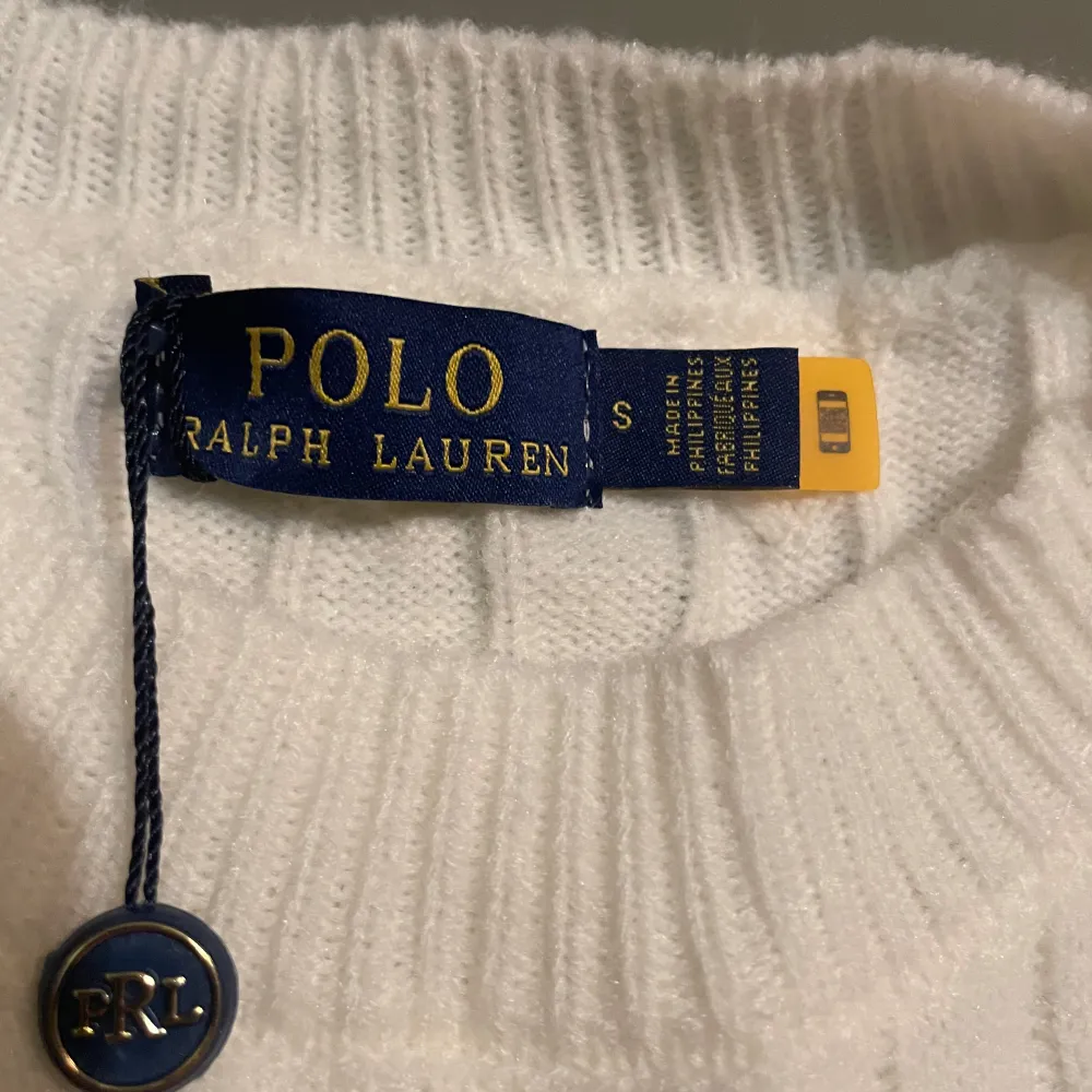 Säljer en stilren vit kabelstickad tröja från Polo Ralph Lauren. Tröjan har en klassisk design med broderad logotyp på bröstet och ribbade muddar. Perfekt för en elegant och avslappnad look. . Neuletakit & Villapaidat.