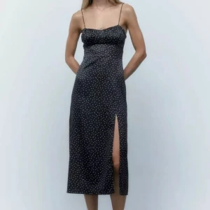 Svart prickig klänning med slits - Snygg svart klänning med vita prickar och slits. Den har smala axelband och snörning i ryggen. Använd fåtal gånger, stretchigt material!