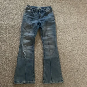 Blå bootcut jeans - Snygga blå bootcut jeans och dekorativa sömmar längs benen. Jeansen har klassiska fem fickor och en knappstängning fram. Perfekta för en avslappnad stil med en touch av retro.