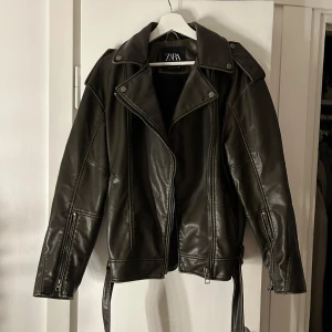 Grön skinnjacka från Zara - Snygg svart skinnjacka från Zara med dragkedja och bälte. Jackan har långa ärmar och en klassisk bikerstil. Oversized i modellen perfekt till vår, sommar, höst 💛