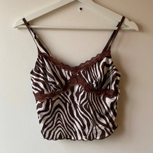 Zebramönstrad linne med spetsdetaljer - Snygg zebramönstrad linne i brunt och vitt med tunna axelband och spetsdetaljer längs kanten. 