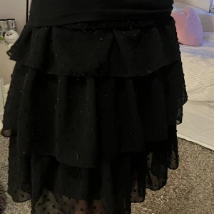 Svart volangkjol med prickar - Snygg svart kjol med volanger och små prickar. Kjolen är perfekt för att ge en chic touch till din outfit. Den är kort och har en elastisk midja för bekväm passform, täcken på användning finns men den är ej sliten och super fin🤍🪩Storlek står ej men skulle säga S/XS då den passar mig