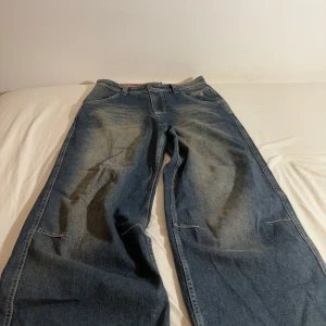 Blå jeansbyxor från Jaded London - Säljer ett par blå jeansbyxor från Jaded London med broderad text 'LDN' på bakfickorna. Byxorna har en loose/baggy passform och är tillverkade i jeansmaterial. Perfekta för en avslappnad stil. (Nypris för jeansen är 1 400 kr.)