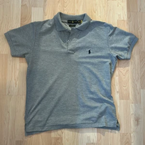 Ralph Lauren Piké - Säljer en klassisk grå pikétröja från Ralph Lauren med korta ärmar och den ikoniska loggan broderad på bröstet. Perfekt för en stilren och avslappnad look!! Skriv för fler bilder!