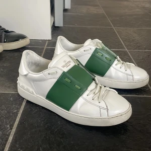 Valentino sneakers i vitt och grönt - Snygga Valentino sneakers i vitt med en grön panel över snörningen. Skorna har en stilren design med diskreta detaljer och är perfekta för en trendig look.