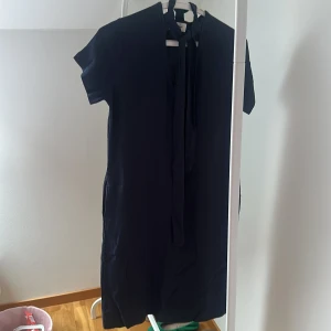 Svart klänning från ottod'Ame - Elegant svart klänning från ottod'Ame med korta ärmar och knytband vid halsen. Perfekt för en stilren look.