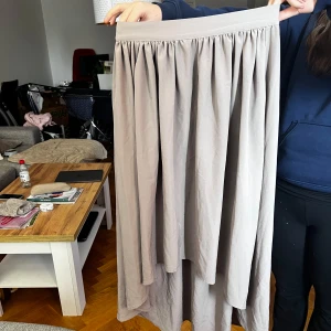 Beige långkjol från Angelology - Säljer en stilren beige långkjol från Angelology. Kjolen har en elastisk midja för en bekväm passform och ett vackert fall. Perfekt för en avslappnad och elegant look. Passar bra till både vardag och speciella tillfällen.