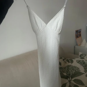 Vit ärmlös klänning - Säljer en elegant vit klänning med smala axelband och v-ringad design. Klänningen har en enkel och stilren look, perfekt för somriga tillfällen. Materialet är lätt och luftigt, vilket gör den bekväm att bära. Aldrig använd 😊