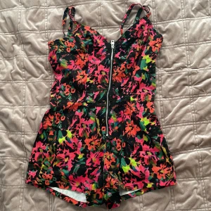 Färgglad blommig jumpsuit från Guess - Säljer en färgglad blommig jumpsuit från Guess med dragkedja framtill. Den har smala axelband och en livfull design i rosa, orange, grön och svart. Perfekt för en somrig look! Köparen står för frakten 💕