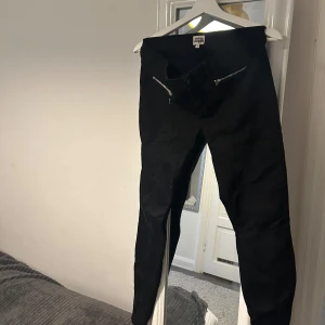 Svarta byxor från Twist & Tango - Snygga svarta byxor från Twist & Tango med dragkedjedetaljer framtill. Byxorna har en tight passform och är perfekta för en stilren look. Snygg slits vid änden av benen. De är tillverkade i ett bekvämt material som ger en skön känsla hela dagen.