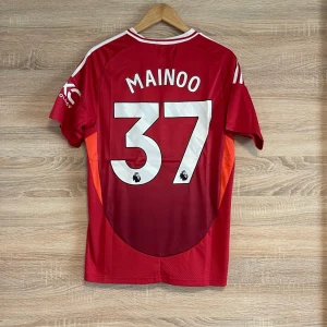 Röd Manchester United fotbollströja - Säljer en röd Manchester United fotbollströja från Adidas med vit text och logga. Tröjan har korta ärmar och nummer 37 med namnet Mainoo på baksidan. Perfekt för fans av laget!