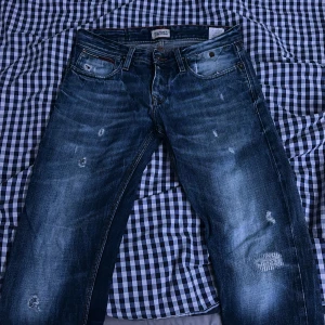 Blå jeans från Hilfiger Denim - Snygga blå jeans från Hilfiger Denim med slitna detaljer och en klassisk femficksdesign. De har en knappgylf och är perfekta för en avslappnad stil. Märkeslogga på bakfickan ger en extra touch.