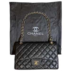 Svart quiltad axelväska  - Elegant svart axelväska  med quiltad design och kedjedetaljer på axelremmen. Väskan har en klassisk CC-logga på framsidan och en röd insida som ger en lyxig känsla. Perfekt för att lyfta vilken outfit som helst.