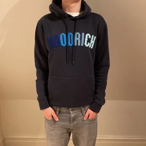 Mörkblå hoodie från Hoodrich - Säljer en snygg mörkblå hoodie från Hoodrich med stor text i blå nyanser på bröstet. Den har en klassisk känguruficka och justerbar huva med snören. Perfekt för en avslappnad stil. Modellen är 170 och det står att tröjan är XS men lutar mer åt S pris är diskuterbart👍