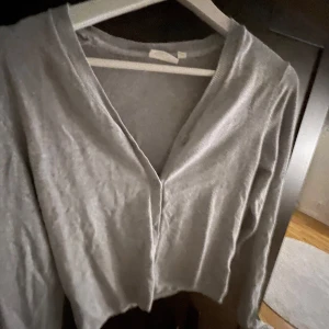 Grå  tröja - Säljer en stilren grå tröja med v-ringning. Tröjan har långa ärmar och en enkel design som passar till många tillfällen. Perfekt för en avslappnad look. Storlek är barn 164 men passar en S väldigt bra