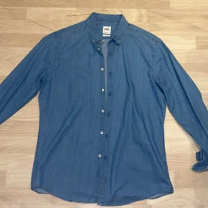 Blå jeansskjorta från Zara - Säljer en stilren blå jeansskjorta från Zara i slim fit. Skjortan har långa ärmar och knappar framtill. Perfekt för en avslappnad men ändå snygg look.