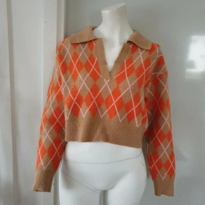 Stickad tröja - Säljer en snygg och trendig beige och orange tröja med argyle-mönster. Tröjan är croppad med långa ärmar och en klassisk krage. Perfekt för en stilren och avslappnad look. 🌟 Har i storlek S och M