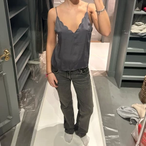 Grå sidenlinne - Säljer ett elegant grått sidenlinne med tunna axelband. Linnet har en slät och glansig yta som ger en lyxig känsla. Perfekt för att klä upp en outfit eller bära som det är för en stilren look.