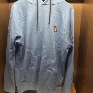 Blå hoodie från Sail Racing - Säljer en snygg blå hoodie från Sail Racing. Den har en klassisk design med en liten logotyp på bröstet och en bekväm huva med dragsko. Perfekt för en avslappnad stil.