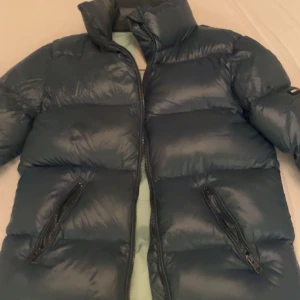 Mörkblå pufferjacka från Tommy Jeans - Säljer en snygg mörkblå pufferjacka från Tommy Jeans. Jätteskönt o varm. Säljer pga att den är för liten. En liten defekt på baksidan(visas på bilden) går säkert att fixa lätt men har ej testat. Storlek xss men passar xs