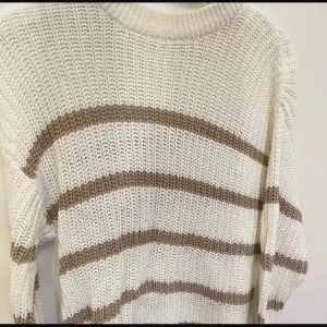 Vit och beige randig stickad tröja - Säljer en supermysig vit stickad tröja med breda beige ränder. Perfekt för kyliga dagar med sin avslappnade passform och långa ärmar. Den är både stilren och bekväm, perfekt för höst och vinter!