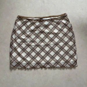 Rutig kjol i beige och brun - Säljer en superfin rutig kjol i beige och brun. Den har en tight passform och är perfekt för både vardag och fest. Kjolen är kort och har en söt volangdetalj längst ner. Perfekt för höst och vår!