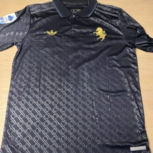 Svart fotbollströja från Adidas - Snygg svart fotbollströja från Adidas med guldiga detaljer och ett lejonemblem på bröstet. Tröjan har korta ärmar och ett diskret mönster över hela tyget. På baksidan finns namnet 'Yildiz' och nummer 10 i guld.