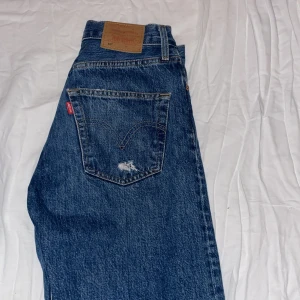 Blå slitna jeans från Levis - Säljer ett par blå slitna jeans från Levis med flera hål och slitningar för en trendig stil. Skulle säga att dom är väldigt baggy/skate i stilen, skit coola och stora för att vara W24 i storlek!! (Har W28). Lite slitningar på kanten vid benen men inget man tänker på.