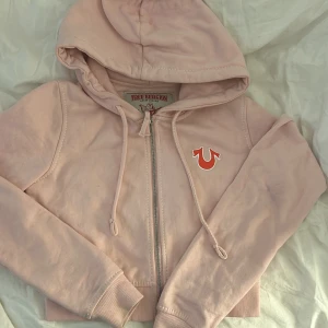 True Religion luvtröja😍 - True Religion luvtröja som är röd och ljusrosa, den är använd bågars få gånger och det är då därför jag säljer den. Den är lite croppad och är storlek S. Den har lite tydligare vita sömmar vid armen. Den är köpt för 999kr.OBS tvättar den innan jag skickar iväg den!!!!💞💞💞