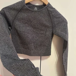 Grå croppad tröja - Säljer en grå croppad tröja med långärmade raglanärmar. Tröjan har en texturerad design och är perfekt för en stilren look. Passar bra till både jeans och träningsbyxor.